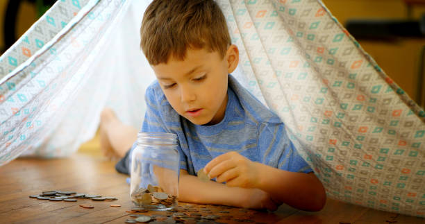 Little boy adding coins to jar. stock photo