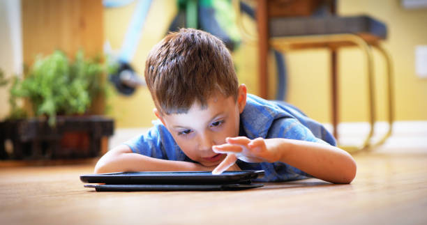istock Little boy using digital tablet laying down on floor inside home. 956515186