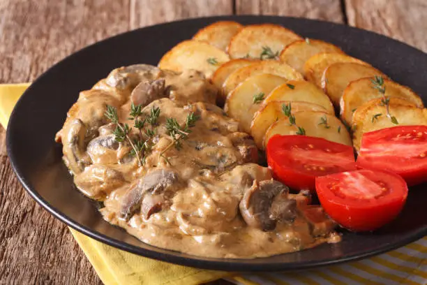 Photo of Diana steak garnished with fried potatoes and fresh tomatoes close-up. horizontal