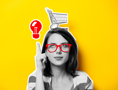 portrait of the beautiful young woman with cart for shopping and red idea bulb on the yellow background. Person lin black and white color style