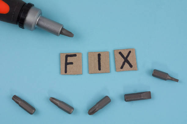 istock One manual screwdriver and five bits for screwdriver near handwritten word FIX on cardboard squares on blue background 956528140