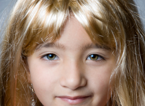 Pretty little girl with green eyes playing with a yellow wig. Girl is an oriental hispanic.