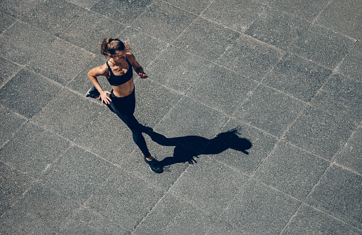 Woman sprinting in the morning outdoors. Top view of female runner working out in the city.