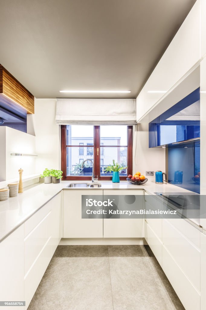 Small bright white kitchen Vertical perspective on a small bright white kitchen interior with a window in the center, elegant countertops and blue modern glass elements Kitchen Stock Photo