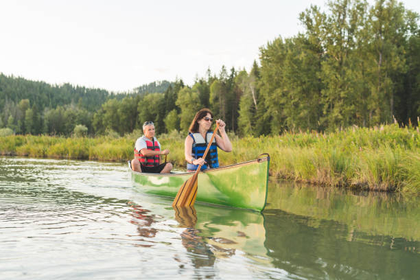 coppia di anziani in canoa insieme intorno a un lago boscoso. - canoeing canoe senior adult couple foto e immagini stock
