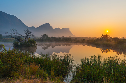 Sunrise inside the Entabeni Game Reserve famous for safari with a reflection of the Hanging Lip of Hanglip mountain peak in a swamp lake located near Kruger Park, Limpopo Province, South Africa.