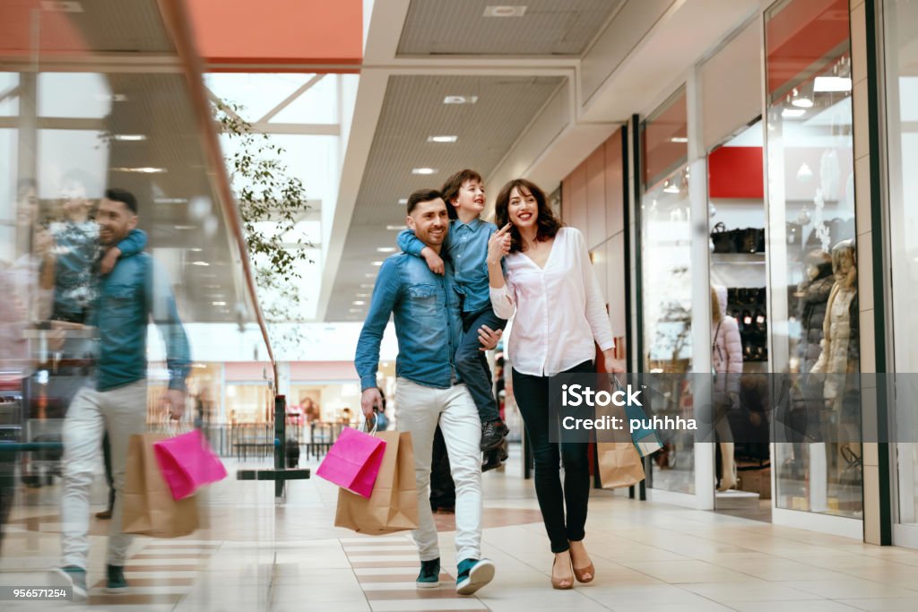 Family Shopping. Happy People In Mall Family Shopping. Happy People With Child Carrying Bags, Walking In Modern Mall. High Resolution. Shopping Mall Stock Photo
