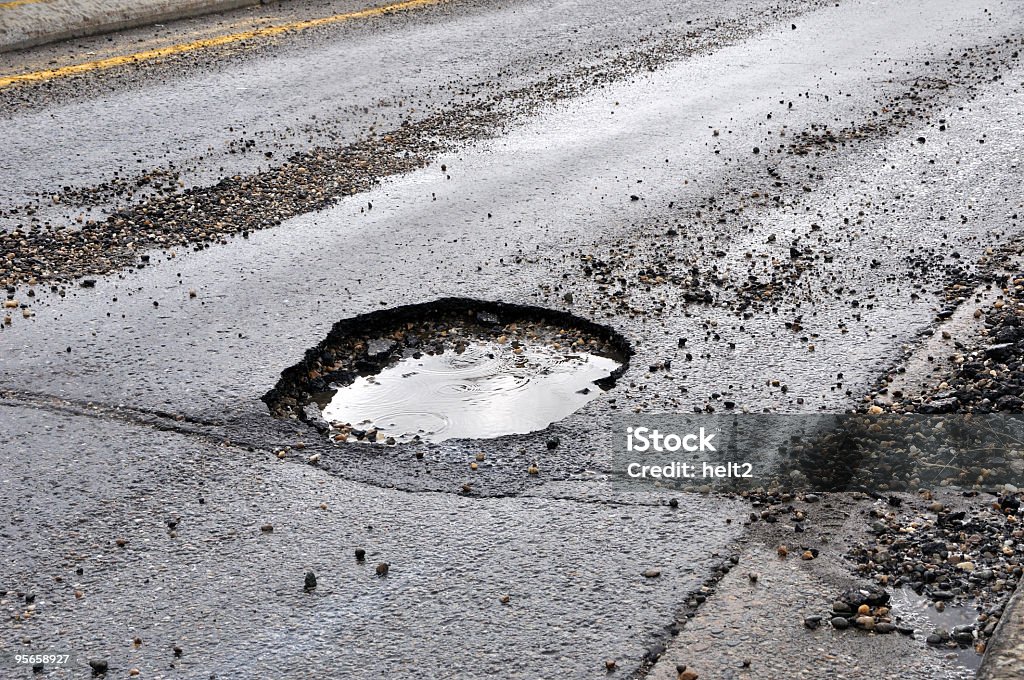 A large pot hole filled with water on an asphalt road A road damaged by rain,snow, or the freeze/thaw cycle that is in need of maintenance. Pot Hole Stock Photo