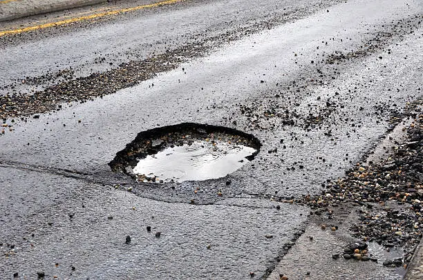 Photo of A large pot hole filled with water on an asphalt road