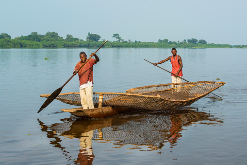 Ndobo, Democratic Republic of Congo - August 27, 2013: Two Congolese fisher man with their typical braided fishing net while paddling in a typical dugout canoe (pirogue).