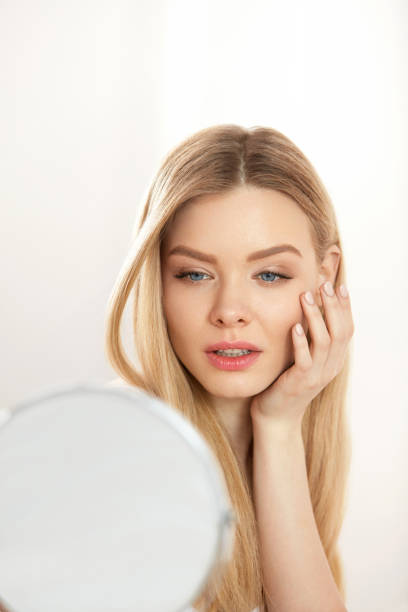 istock Makeup And Beauty. Female Touching Face Skin Looking In Mirror 956605470