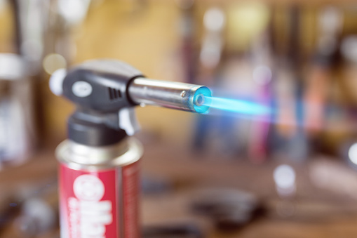Gas cartridge gun lighter .Close-up nozzle of burner with blue flame jet. Workshop background, scorching of wood.