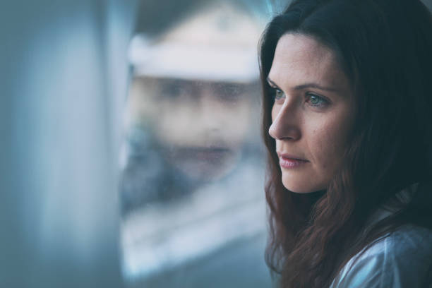 istock Young woman looking through window with reflection 956631858