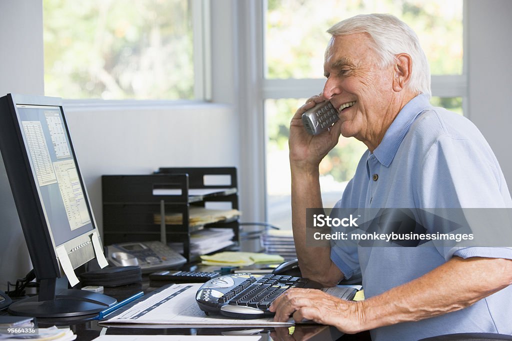 Hombre sonriente por teléfono usando ordenador - Foto de stock de Tercera edad libre de derechos