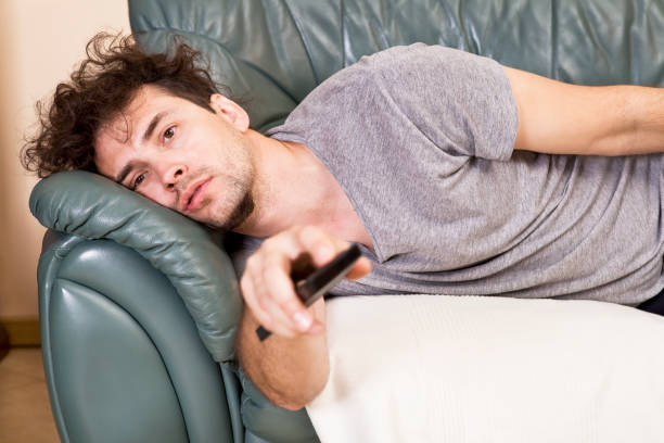 un hombre joven ve televisión y cambia de canales mientras se relaja - television boredom men sofa fotografías e imágenes de stock