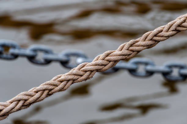 istock Rope and chain with watersurface reflections in the background at daylight. 956657506