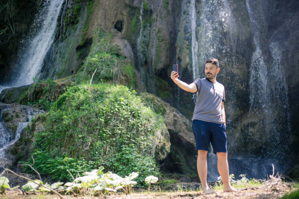 istock man in front of waterfall take selfie 956658288
