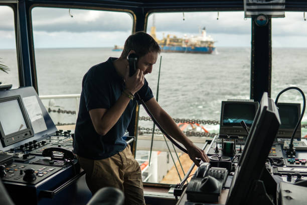 Deck navigation officer on the navigation bridge. He looks through binoculars Deck navigation officer on the navigation bridge. He speaks by VHF radio, GMDSS Watchkeeping, collision prevention at sea. COLREG sea bridge stock pictures, royalty-free photos & images