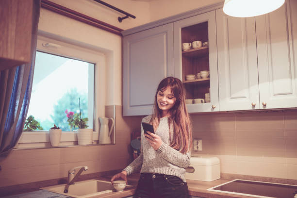 istock Cute Female in Kitchen Drinking Coffee and Texting on Mobile 956675590