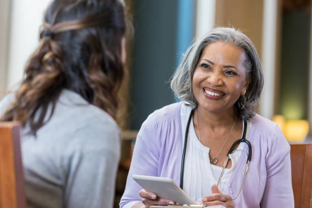 Senior medical professional interviews potential new hire A cheerful senior woman wears a stethoscope as she sits with an unrecognizable woman during an interview.  She holds a digital tablet. medical student photos stock pictures, royalty-free photos & images