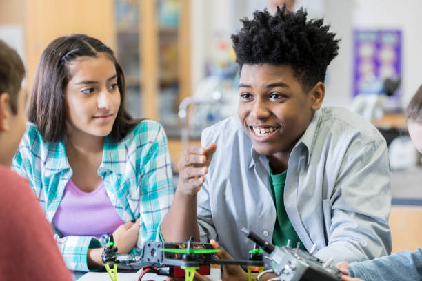 istock Teenage boy discusses project with classmates in robotics lab 956728510