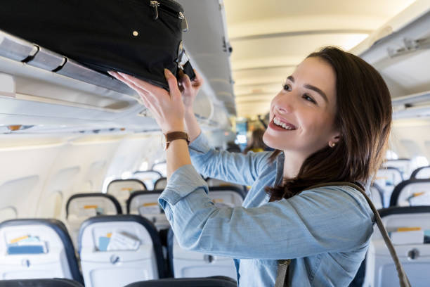 Woman places luggage in airplane's overhead compartment Confident female business traveler places a carryon luggage item in an overhead compartment. hand luggage stock pictures, royalty-free photos & images