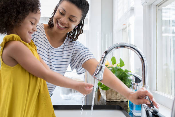 istock Mom and daughter wash hands in kitchen sink 956729648