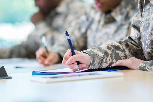 Unrecognizable soldiers take notes in class while in college. Focus is on the hand writing in a note book.