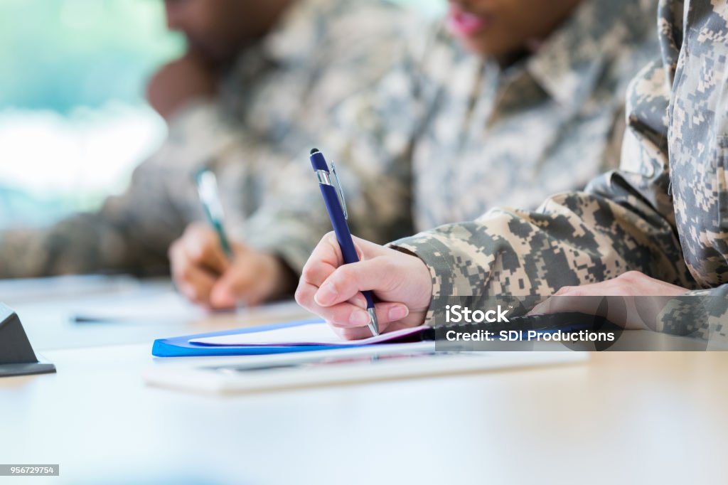 Unrecognizable veterans take a college course Unrecognizable soldiers take notes in class while in college. Focus is on the hand writing in a note book. Military Stock Photo
