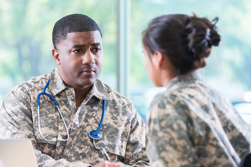 Serious army healthcare professional talks with a female soldier patient.