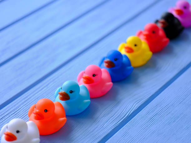 ligne de caoutchouc générique multicolore arc-en-ciel canards, émouvant dans une conduite ordonnée, posez sur une table à grains en bois bleue. - grained photos et images de collection