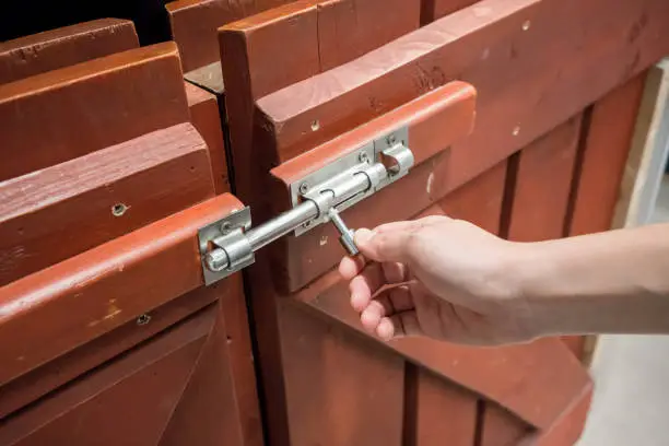 Woman hand pulling latch lock of the brown wooden fence for safety.