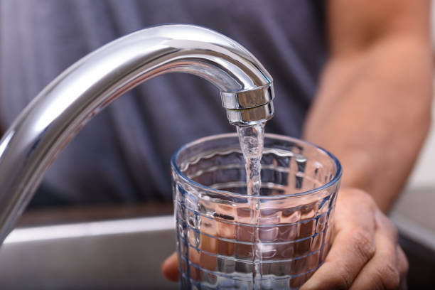 istock Hand with drinking glass filling water from kitchen faucet 956769978