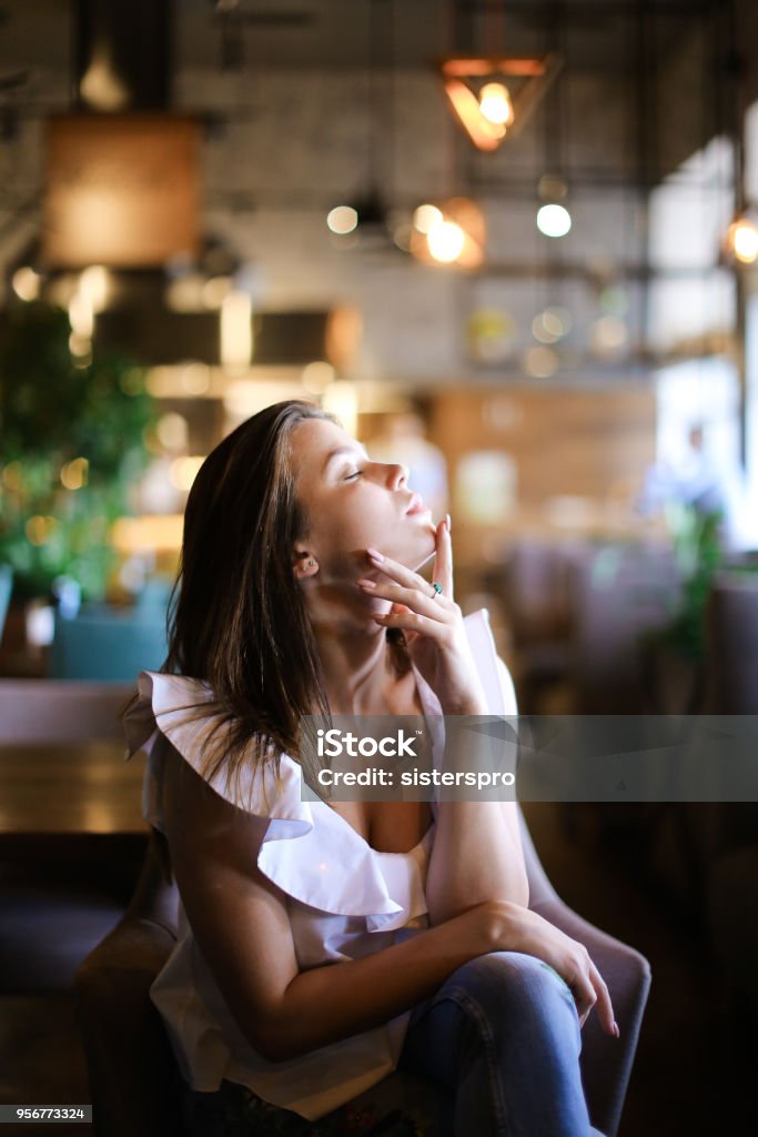 Relaxed female person sitting at cafe and wearing silver ring with emerald and ethnic jeans Relaxed woman sitting at cafe and wearing silver ring with emerald ethnic jeans. Concept of fashion and beauty. Adult Stock Photo