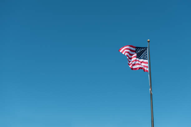 istock American flag waving against solid modern style blue sky, positioning on the right side 956774496