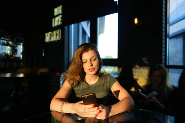 istock Young woman using smartphone and sitting at cafe in sun rays 956778824