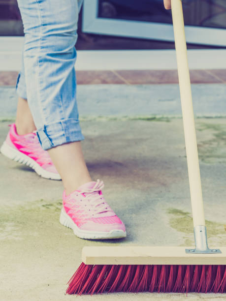 istock Woman using broom to clean up backyard patio 956787080