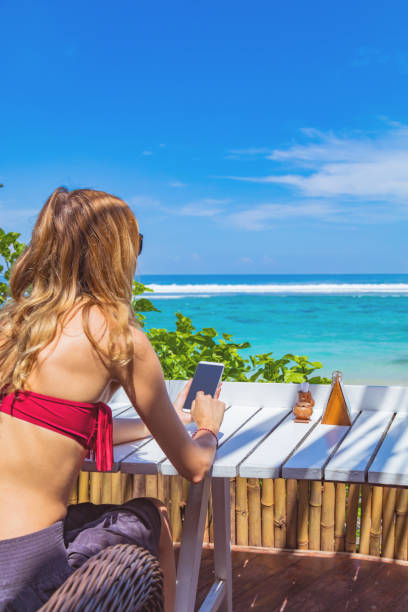 istock Girl using cellphone in the restaurant on a exotic tropical beach. 956797534