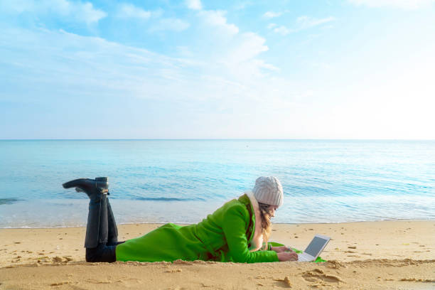 istock Green dressed woman using Laptop on the beach seaside sunset on winter 956800032