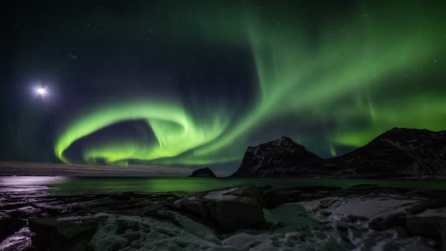 Time lapse tracking shot of Northern Lights, polar light or Aurora Borealis in the night sky over the arctic ocean of the Lofoten islands in northern Norway.