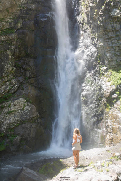 istock Young woman admires waterfall in mountains 956808912