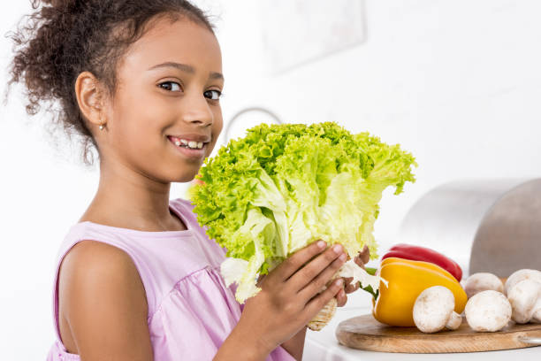 istock smiling african american child holding green fresh lettuce in kitchen 956813006
