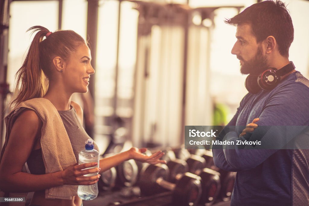 Talk after exercise. Smiling young athlete girl refreshing after training and talking with trainer. Fitness Instructor Stock Photo