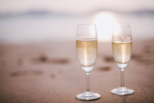 Two champagne glasses on the beach at sunset.