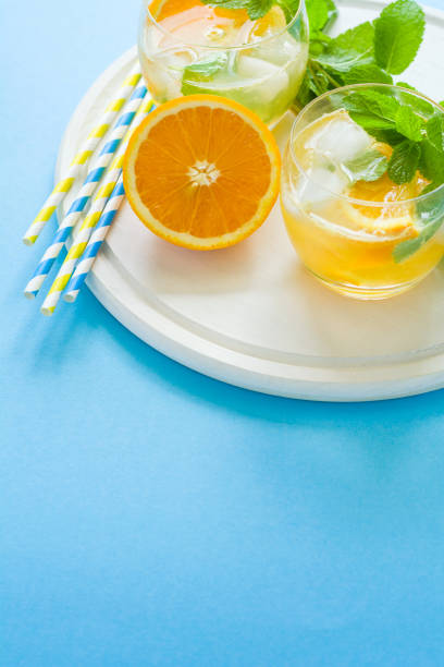 Orange lemonade with slices of orange, ice and mint on blue background.