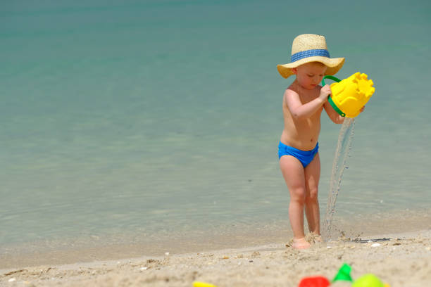 Two year old toddler boy playing with beach toys on beach
