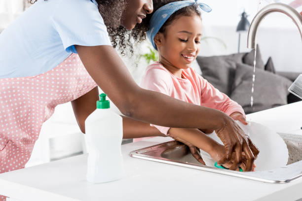 african american mother and daughter washing dishes with detergent on kitchen african american mother and daughter washing dishes with detergent on kitchen washing dishes photos stock pictures, royalty-free photos & images