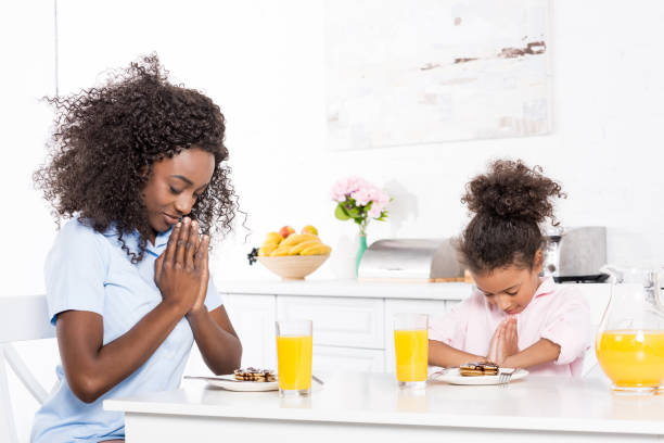 istock african american mother and daughter praying before breakfast in kitchen 956819518