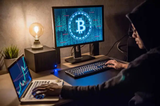 Photo of Hacker man using laptop and computer with Bitcoin green binary graphic and cryptocurrency candlestick graph price on monitor screen