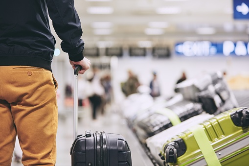 Man traveling by airplane. Young passenger holding his suitcase near baggage claim in airport terminal.